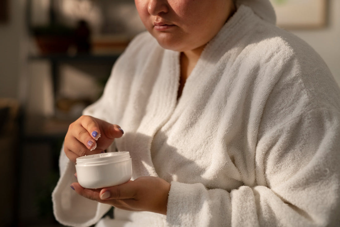 Woman in a bathrobe scooping All In One Butter moisturizer from its jar