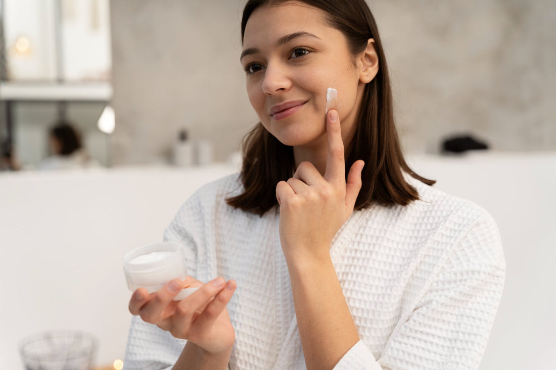 Woman applying face moisturizer cream to her cheek while holding the jar