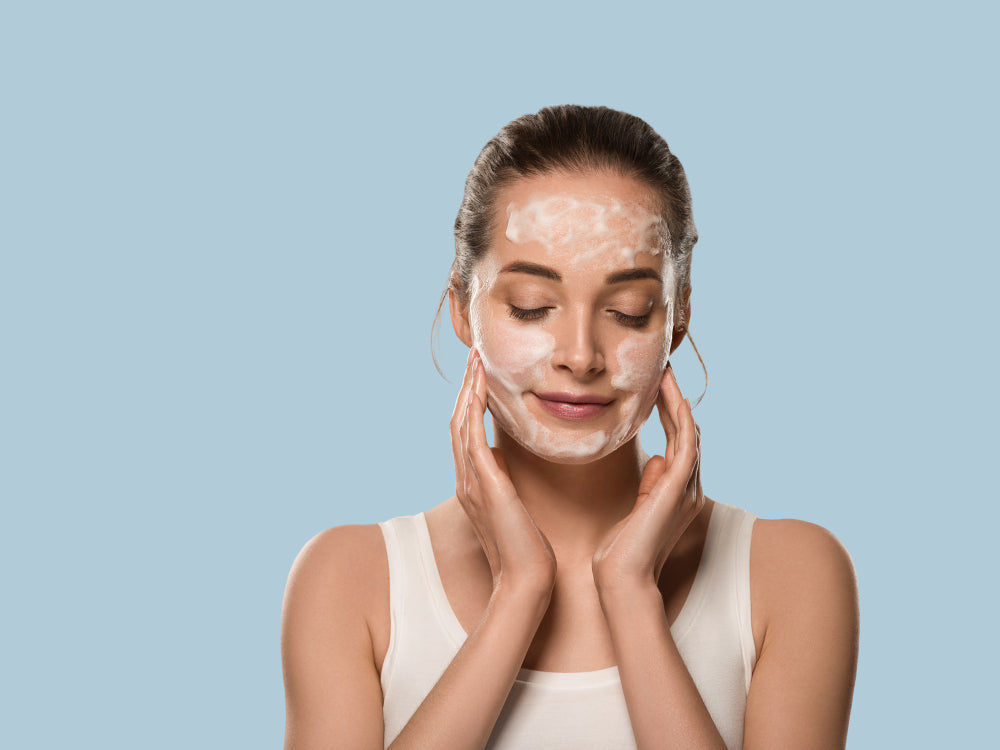 Woman applying a cleansing balm foam to her face against a blue background