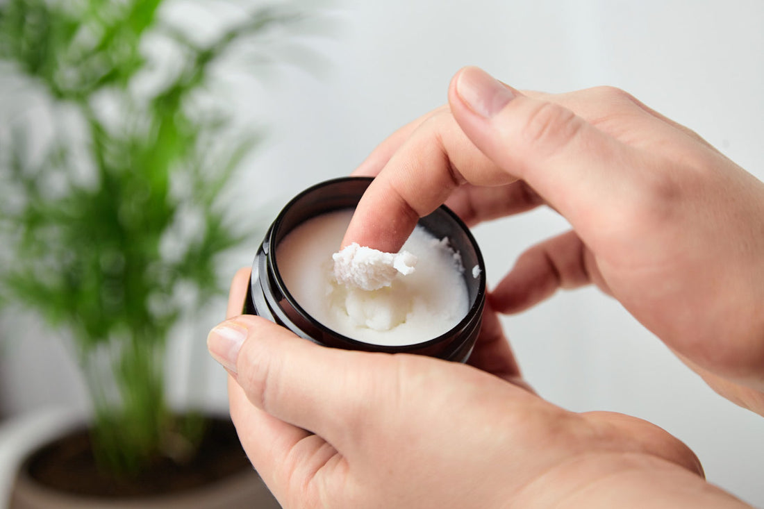 Hands scooping All In One Butter moisturizer from its jar