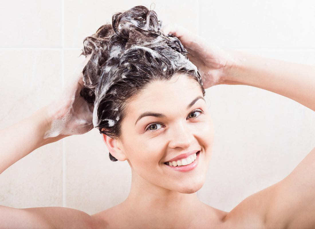 Smiling woman washing her hair with rosemary shampoo in the shower