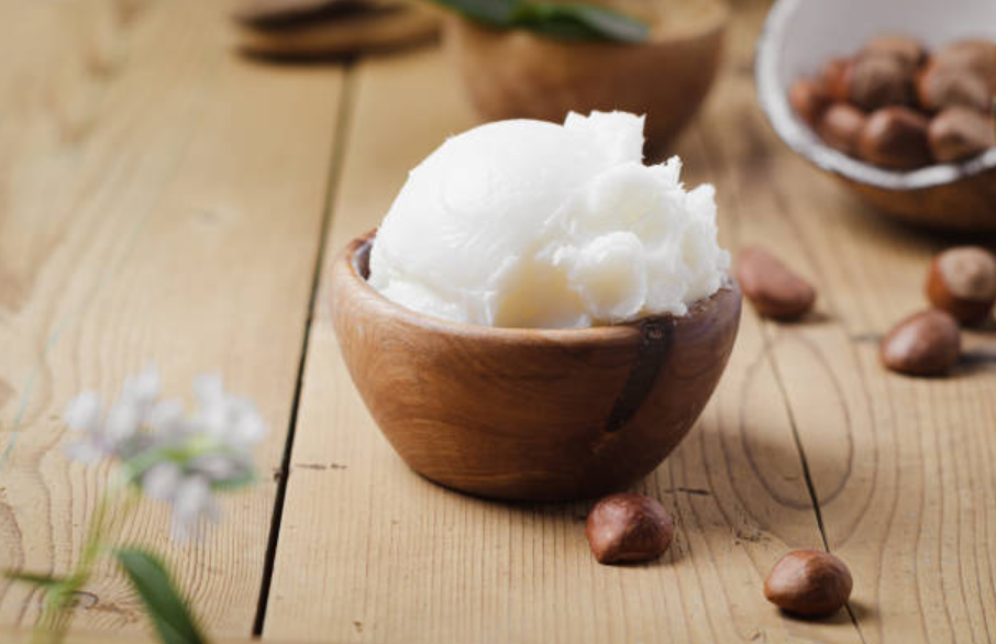 Scoop of raw shea butter in a wooden bowl surrounded by shea nuts