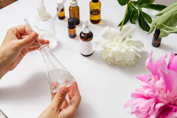 Hands mixing natural hair oil ingredients among flowers and amber glass bottles